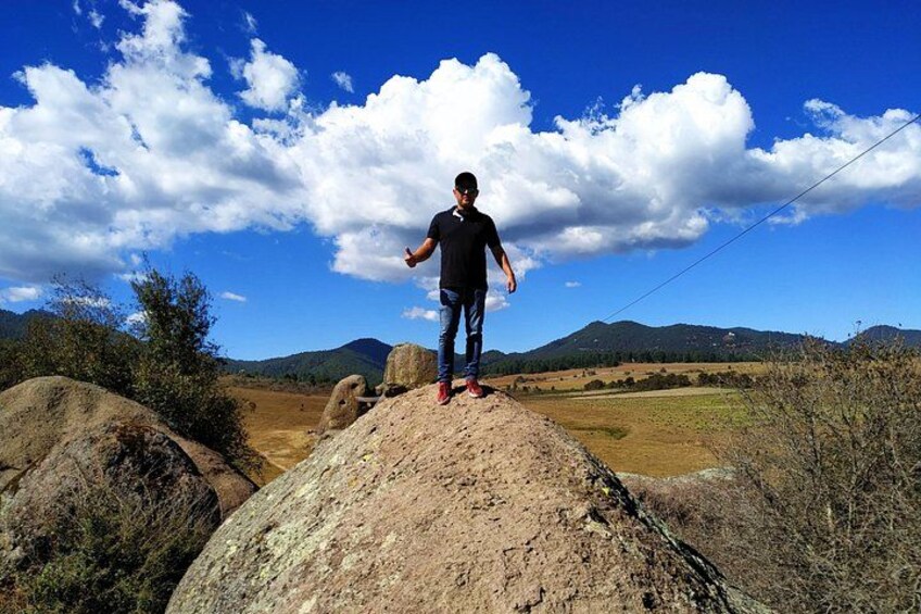 A person standing on a rock with a clear blue sky and mountains in the background. 2