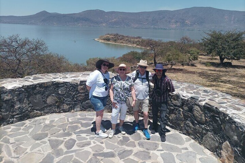 A group of people standing on a stone platform with a lake and mountains in the background. 4