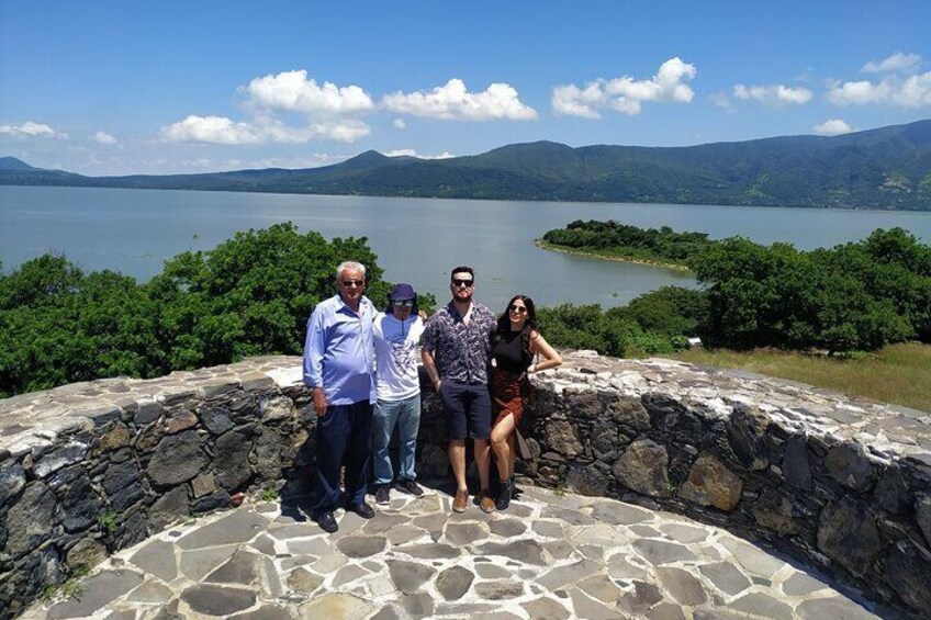 A group of people standing on a stone platform overlooking a lake with mountains in the background. 1