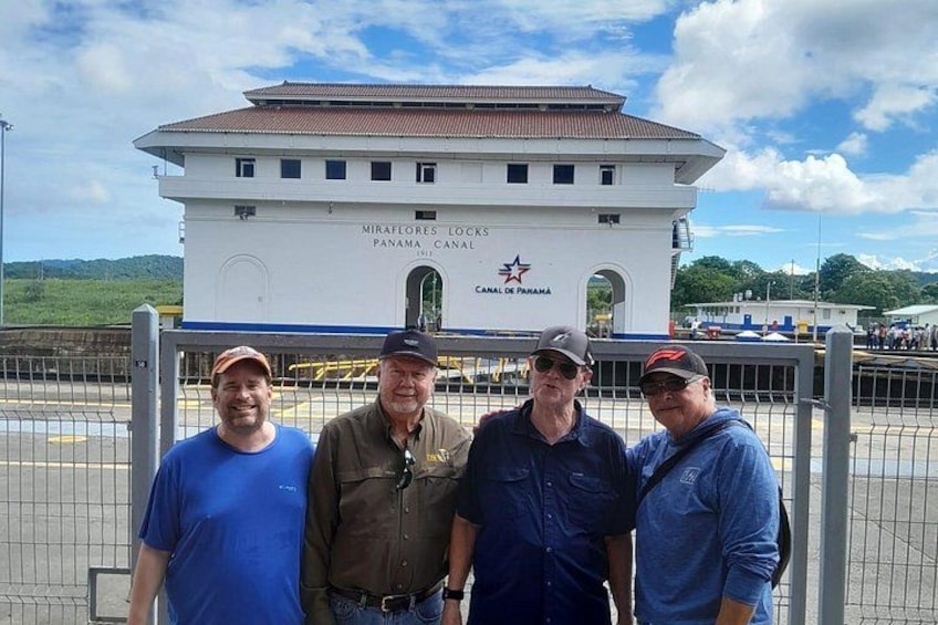 A group of people standing in front of a building with the text 'MIRAFLORES LOCKS CANAL DE PANAMA' and a star emblem. 3
