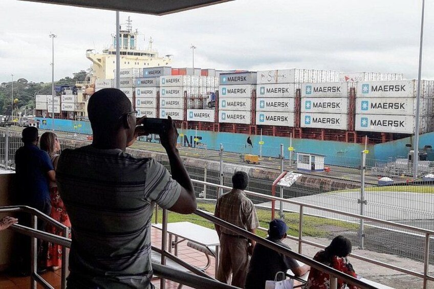 A man taking a photo of a cargo ship with multiple containers labeled 'MAERSK' in a port. 5