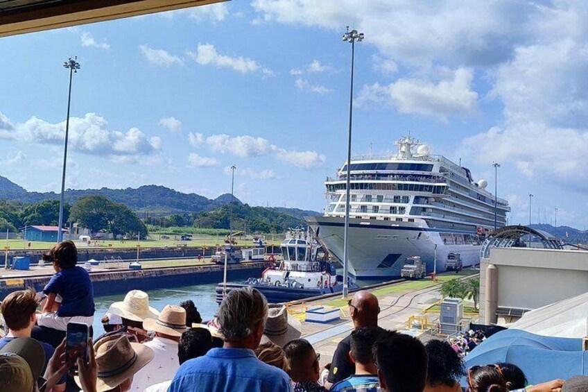 A large cruise ship docked at a port with people observing from the dock. 2