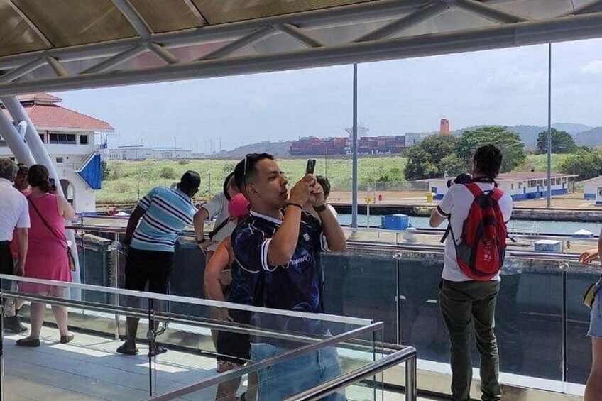 People on a boat deck, some taking photos, with a view of a river and distant buildings. 5
