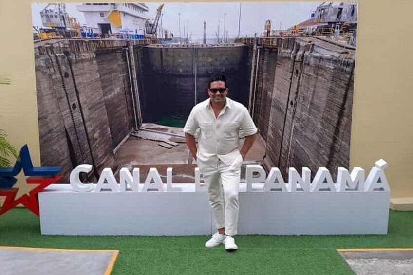A man standing in front of a large sign that reads 'CANAL DE PANAMÁ' with a backdrop of a canal and ships. 3
