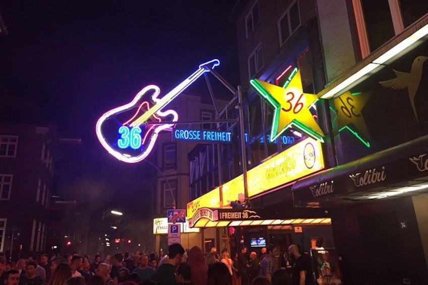 Une enseigne au néon en forme de guitare, une autre en forme d’étoile, et une foule de personnes dans une rue de la ville, de nuit. 1