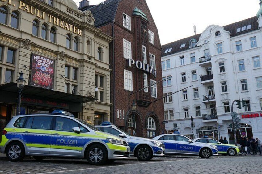 Una calle con coches de policía estacionados frente a un teatro y un edificio con la palabra 'POLIZEI'. 3