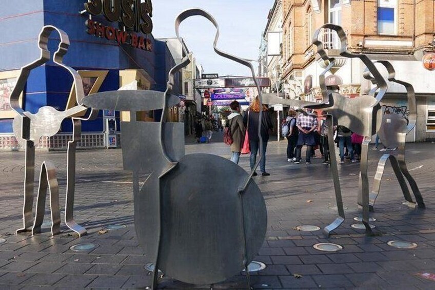 Una plaza pública con esculturas metálicas abstractas y un edificio con un letrero que dice 'SUSIS SHOW BAR'. 2