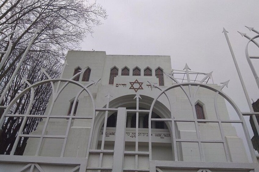 Un edificio con una estrella de David y texto hebreo, rodeado por una cerca blanca con parte superior arqueada. 5