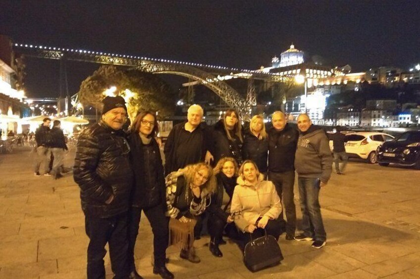 Un grupo de personas posando en una plaza pública por la noche, con edificios iluminados y un puente al fondo. 3