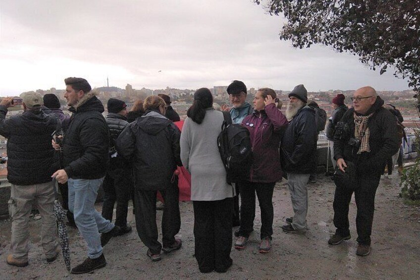 Un grupo de personas está de pie sobre un afloramiento rocoso con vista a un paisaje urbano. 4