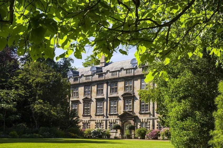 Un grand bâtiment historique, doté de nombreuses fenêtres et d’une entrée centrale, et entouré d’une végétation luxuriante et d’arbres. 1