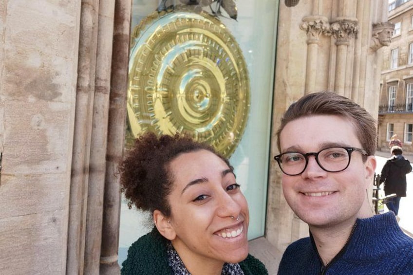 Deux personnes se tiennent devant une grande porte richement décorée, ornée d’un motif circulaire. 2