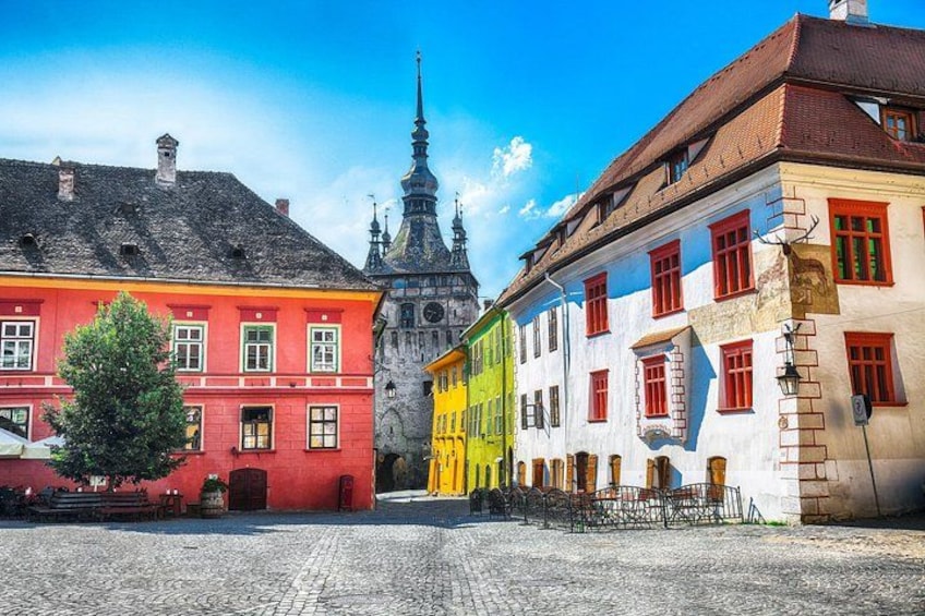 A cobblestone street with colorful buildings, a church spire, and a tree. 1