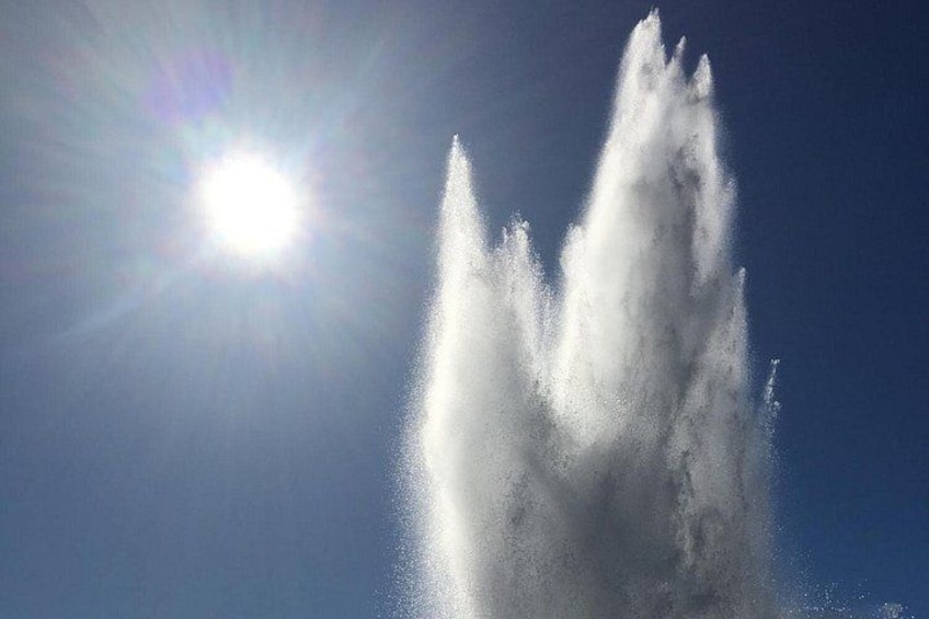 Ein sonnendurchfluteter Brunnen mit Wasserstrahlen vor blauem Himmel. 1