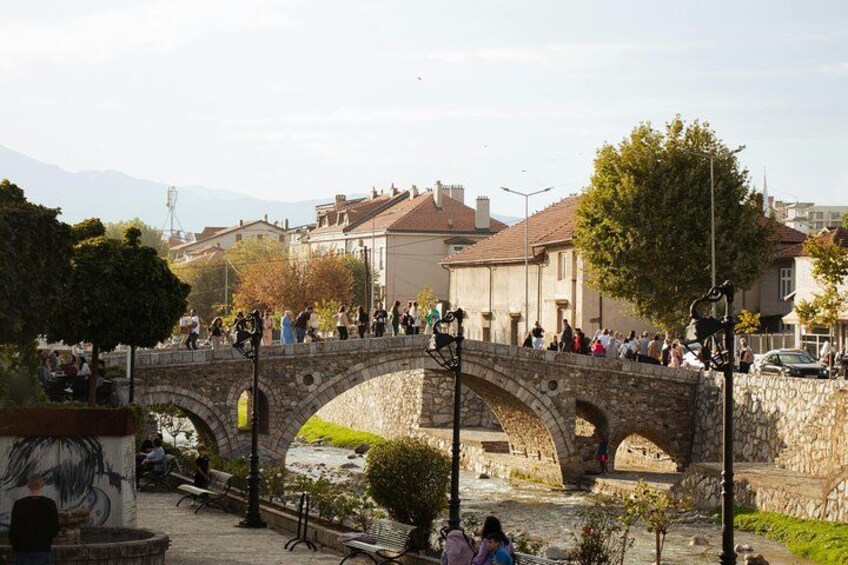 A stone bridge with people walking across it, surrounded by trees and buildings. 2