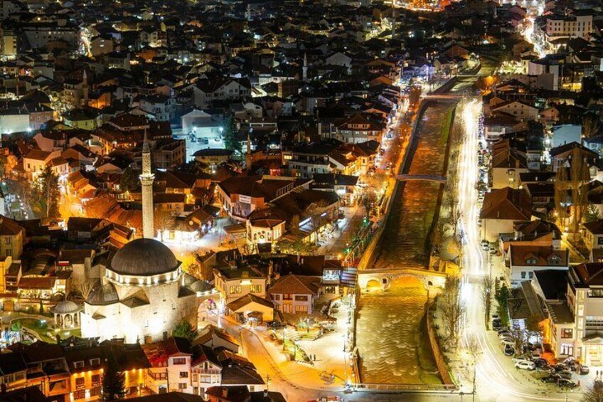 A nighttime aerial view of a city with a prominent tower, a river, and illuminated streets. 3