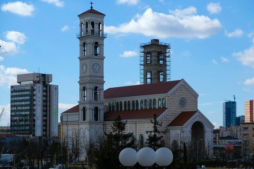 A historic church with a bell tower and scaffolding, surrounded by modern buildings. 5