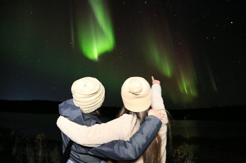 Two people embracing, facing a night sky with green aurora borealis. 3