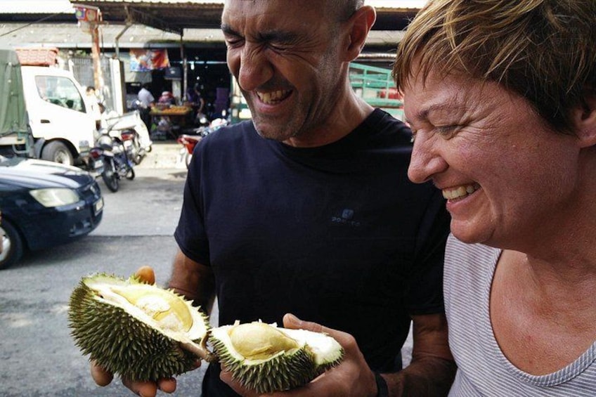 Two people holding a durian fruit in an outdoor market setting. 2