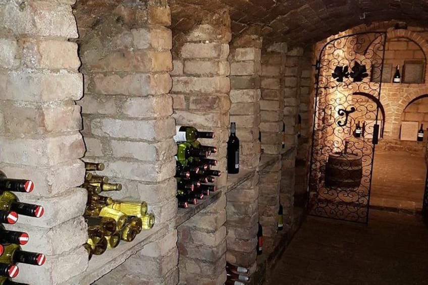 A wine cellar with stone walls and shelves holding wine bottles. 3