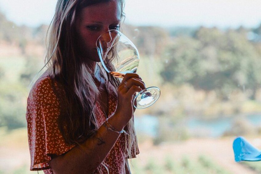 Una persona sosteniendo una copa de vino, vistiendo una camisa de lunares, con un paisaje natural desenfocado al fondo. 2