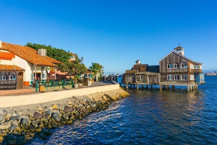 A coastal town with a wooden pier, a stone wall, and buildings with red-tiled roofs. 2