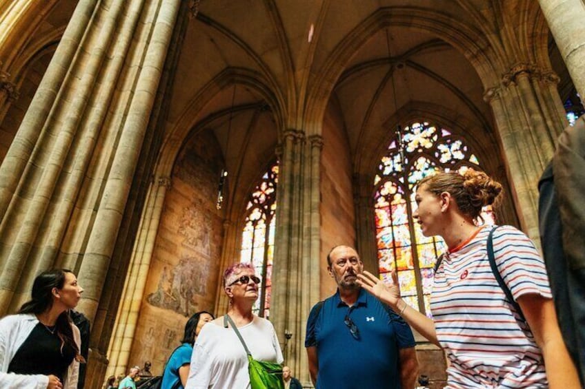 Een groep mensen in een kathedraal met gotische architectuur, herkenbaar aan puntbogen en gebrandschilderde ramen. 1