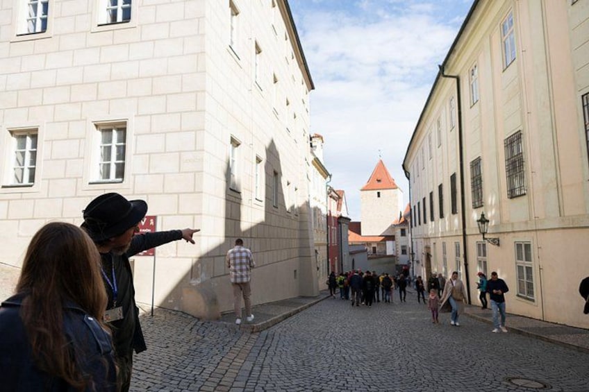 A cobblestone street lined with historic buildings, a group of people walking, and a tower in the background. 4