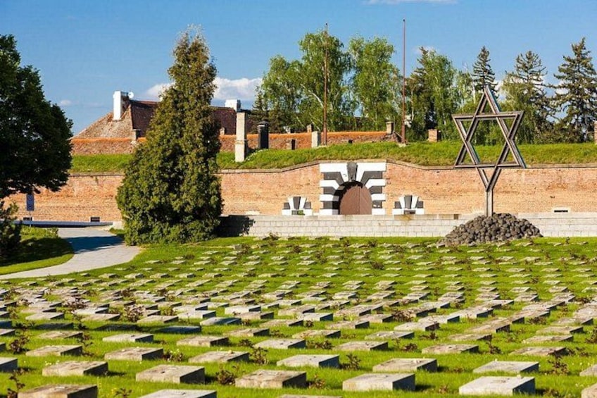A cemetery with numerous headstones, a Star of David, and a building in the background. 1