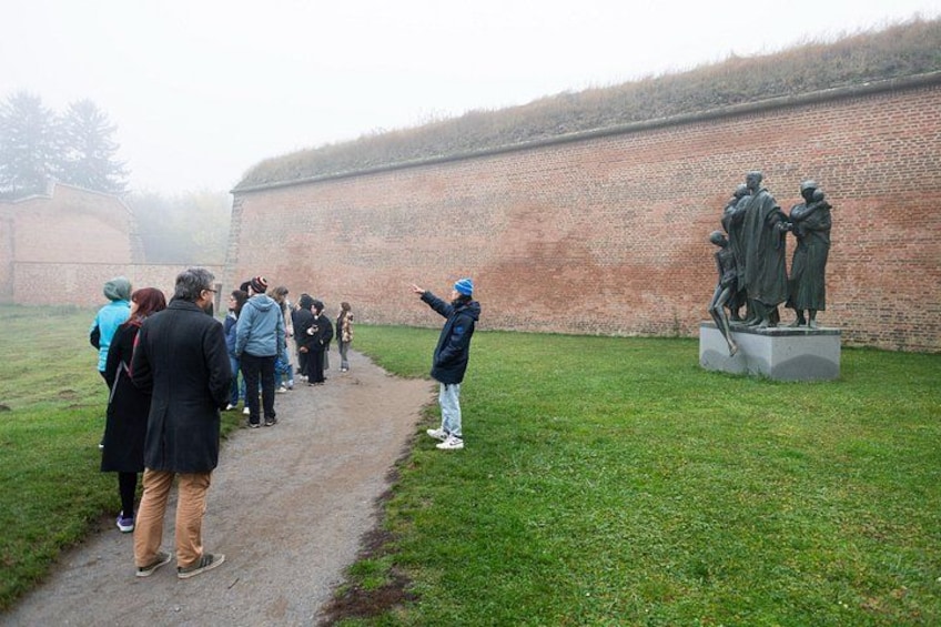 A group of people walking along a path in a grassy area with a brick wall and a statue in the background. 3