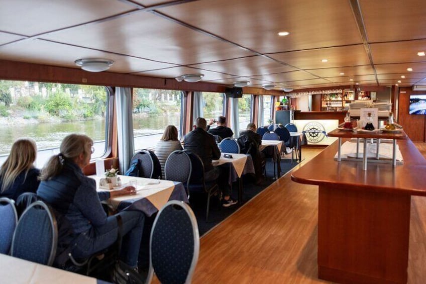 A dining area on a cruise ship with tables and chairs, a bar, and a view of the river outside. 5