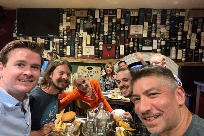 Un grupo de personas cenando en un restaurante con una pared de botellas de vino al fondo. 1