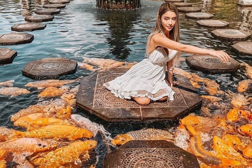 Una mujer con vestido blanco sentada sobre una plataforma de piedra estampada rodeada de agua y peces. 5