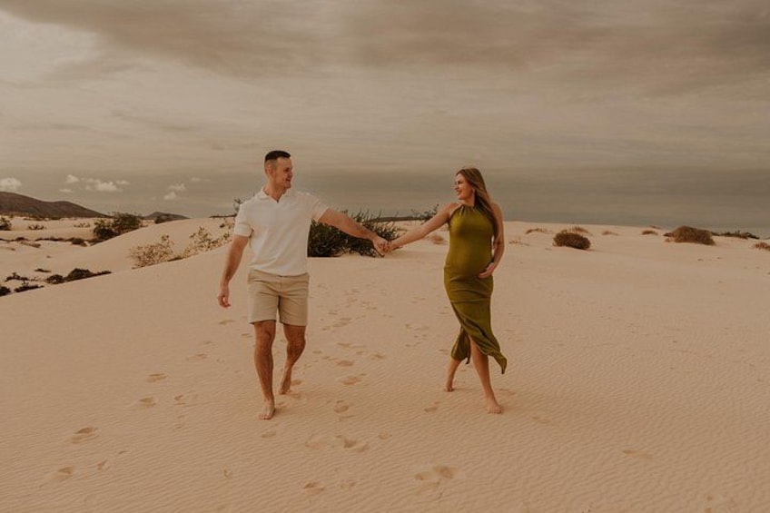 Two people walking on a sandy beach with footprints, holding hands, and a cloudy sky in the background. 4