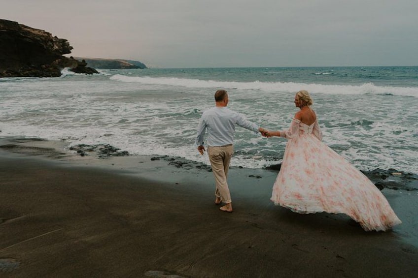 A couple walking on a beach with waves crashing onto the shore. 2