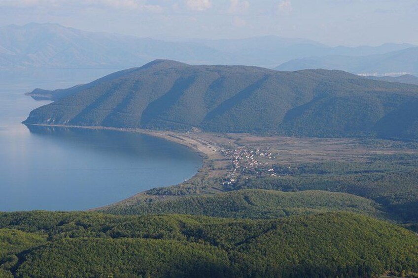 Ein See, umgeben von bewaldeten Hügeln, einer kleinen Siedlung und einem fernen Gebirge. 5