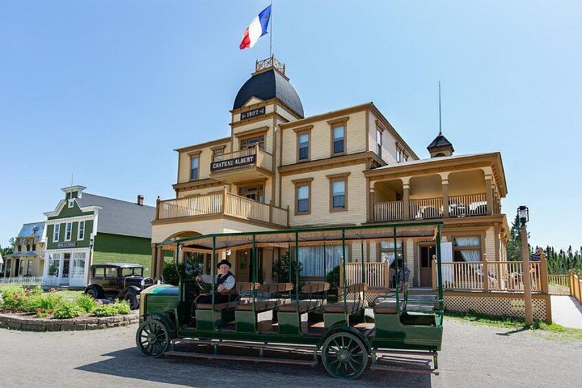 A vintage green trolley in front of a large building with a French flag. 1