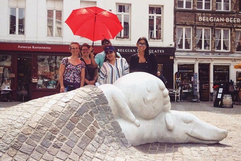 Eine Skulptur einer liegenden Figur auf einem Kopfsteinpflasterbelag, hinter der sich Personen befinden. 4