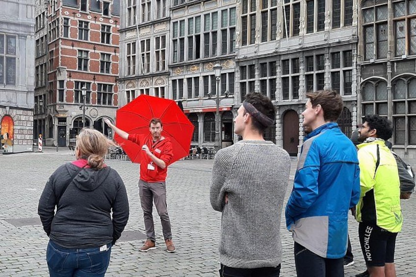 Eine Kopfsteinpflasterstraße mit historischen Gebäuden, einer Person mit einem roten Regenschirm und mehreren Fußgängern. 2