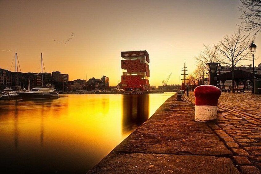 A waterfront with a red and white bollard, a boat, and buildings reflecting on the water. 2