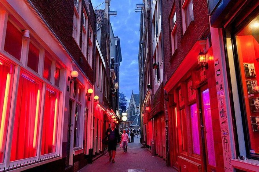 A narrow street with buildings on either side, illuminated by red and pink lights. 1