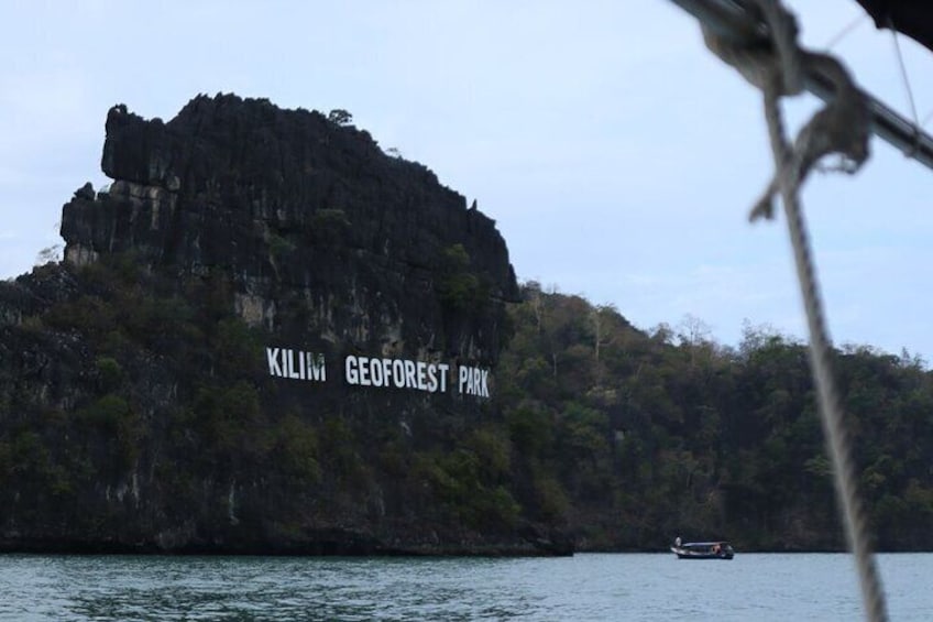 A large rock with 'Kilim GeoForest Park' written on it, surrounded by water and greenery. 3