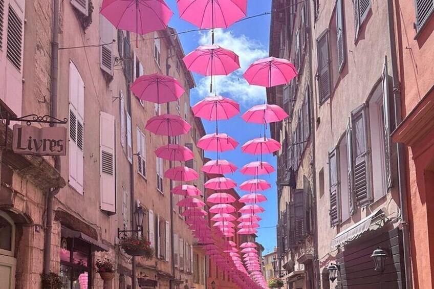 A street with pink umbrellas hanging from the buildings. 1