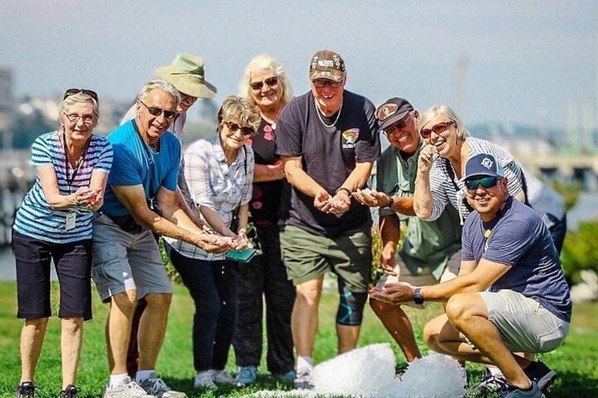 A group of people participating in an outdoor activity, possibly a team-building exercise, in a grassy area with a clear sky. 2