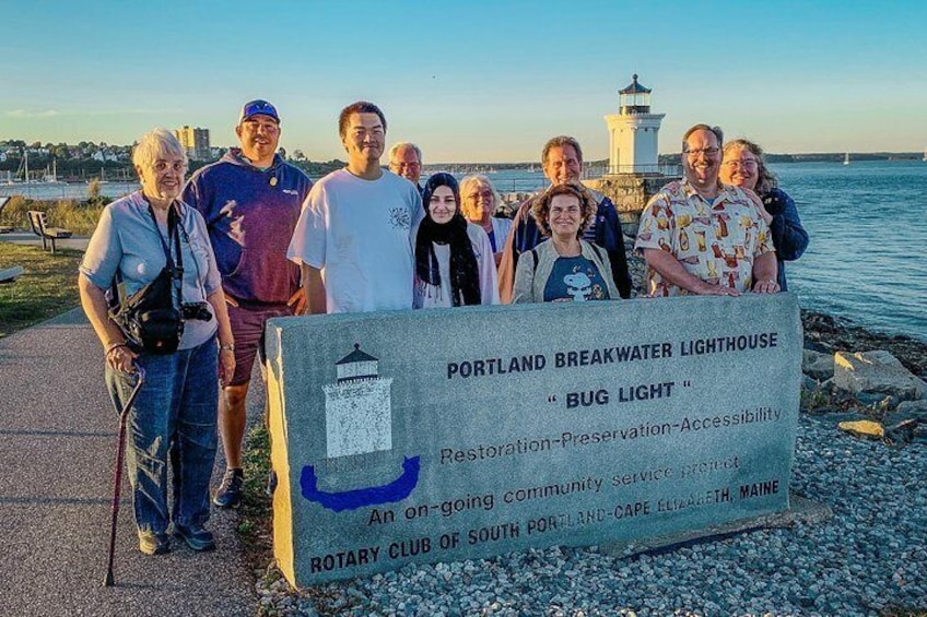 En gruppe mennesker står foran et skilt med Portland Breakwater Lighthouse. 5