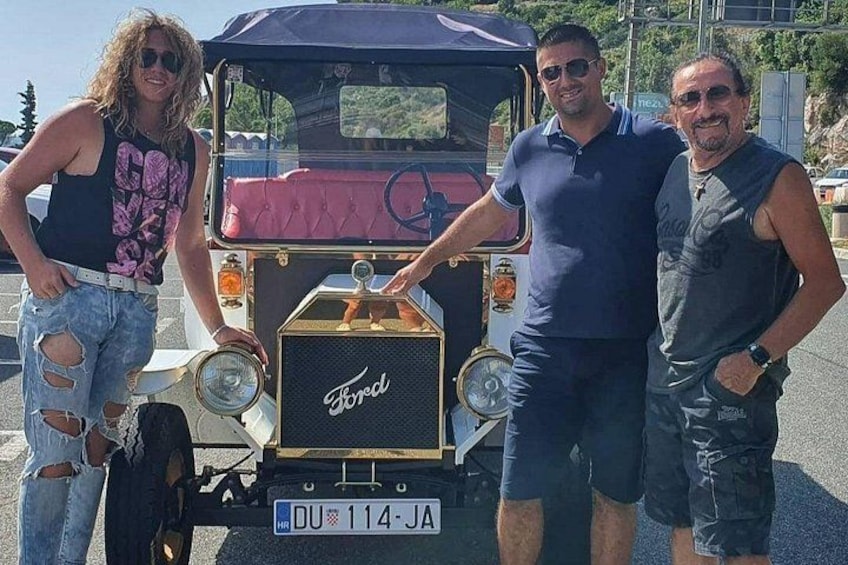 Three people standing in front of a vintage Ford vehicle with a license plate DU 114-JA. 4