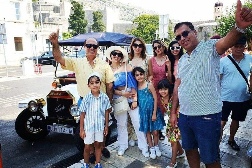 A group of people posing with a vintage car on a city street. 5