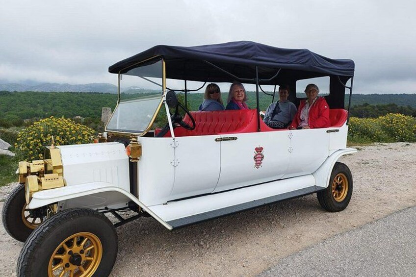 A vintage car with a black roof, passengers, and a countryside landscape. 1