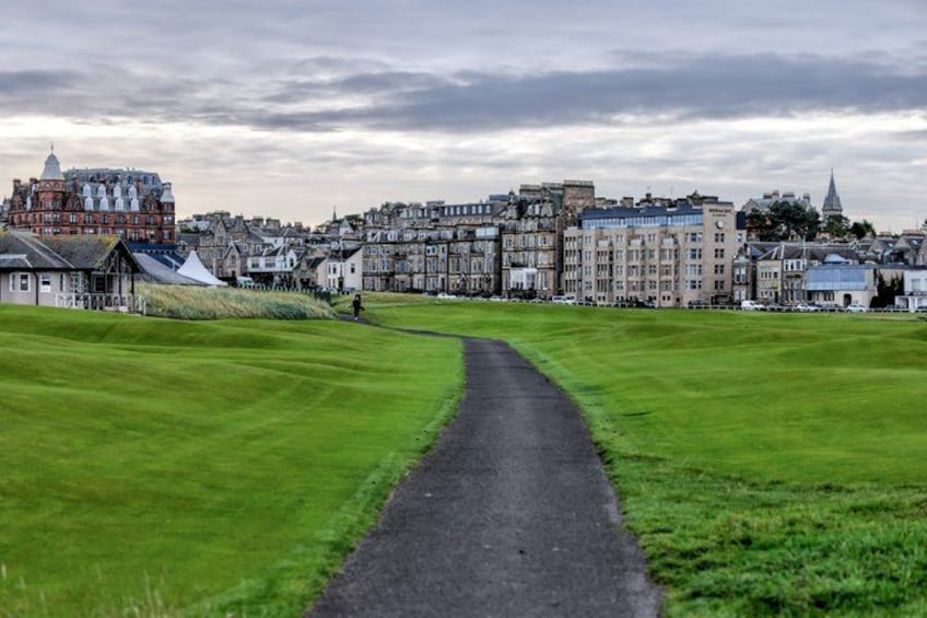 A pathway leading through a green field towards a historic town with buildings. 4