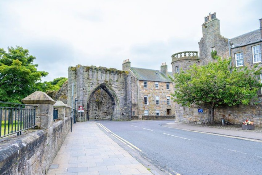 A stone archway leading to a historic building with a paved sidewalk and a road. 2